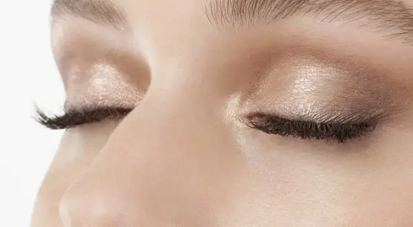 Occhi chiusi con trucco luminoso, ciglia lunghe e folte. Uno sguardo spento che riflette un momento di quiete interiore.