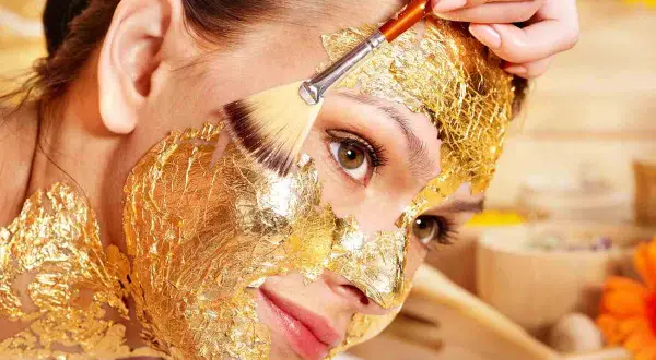Una donna riceve un trattamento di bellezza con una maschera viso oro, scoprendo i suoi benefici rigeneranti.