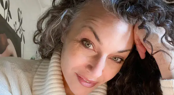 Donna con capelli ricci e grigi, che riflette sulle cause della ricrescita capelli bianchi troppo veloce.