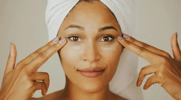 Donna con turbante applica crema contorno occhi, mostrando la differenza tra unguento e crema per la cura della pelle.