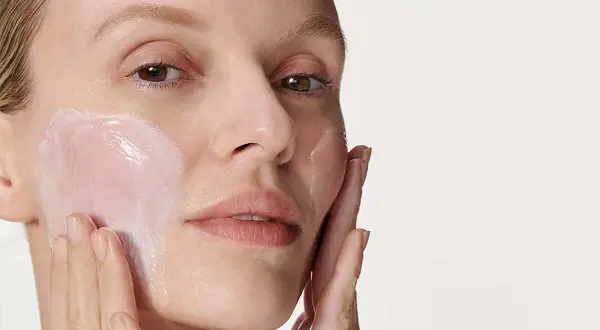 Donna applica una crema idratante sul viso. La sua pelle appare luminosa e sana, pronta per il giorno. Prima scrub o detergente? La scelta è tua per una pelle perfetta.