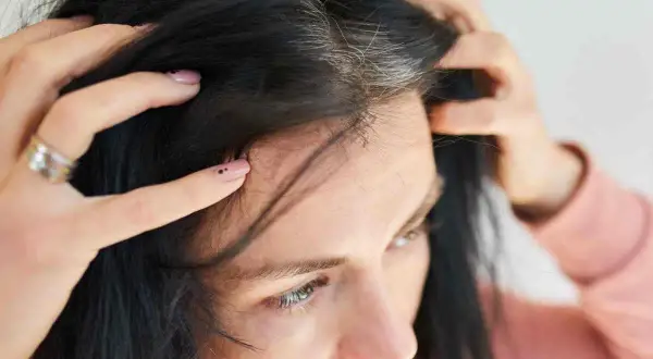 Mani che toccano capelli scuri con ciocche bianche, un segno di come cambiano i capelli nel tempo.