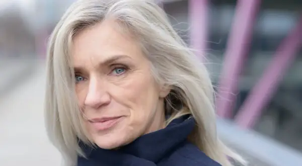 Donna con capelli biondo cenere, un sorriso discreto e occhi azzurri. Nonostante i capelli bianchi, il suo look è curato, quasi a voler camuffare capelli bianchi con un'eleganza naturale.