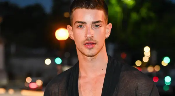 Uomo con capelli spettinati, sguardo intenso e un leggero sorriso. Indossa una veste trasparente nera.