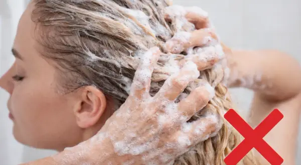 Mani che massaggiano shampoo sui capelli biondi, con una croce rossa che indica di evitare certi rimedi capelli grassi.