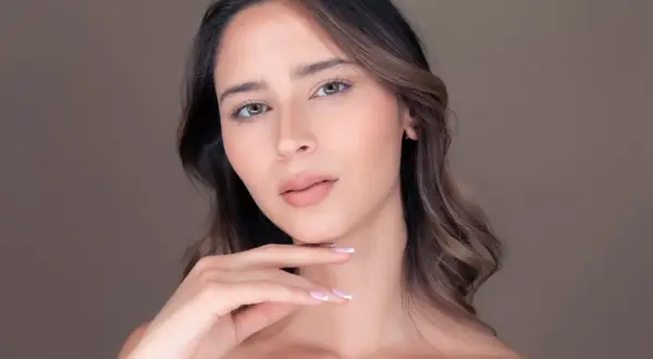 Viso di donna con pelle luminosa, effetto di retinolo e acido ialuronico. Mano sfiora il mento.