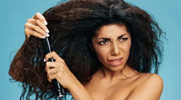 Donna con capelli crespi prova a usare una piastra, sperando in un trattamento anti crespo efficace.