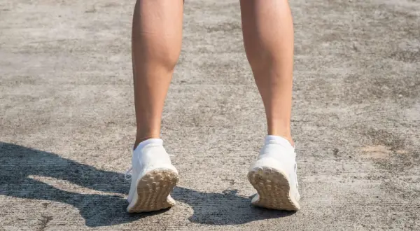 Gambe di donna con polpacci grossi, forse a causa di allenamento intenso. Scarpe da ginnastica bianche su cemento.