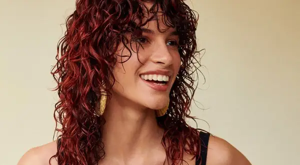 Donna sorridente con splendidi capelli mogano ricci e bagnati, che le incorniciano il viso.