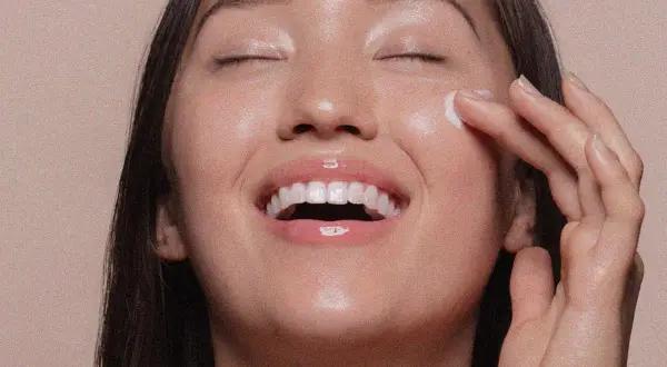 Viso radioso di una donna che applica una crema, un gesto che ricorda cos'è lo scrub per una pelle luminosa e liscia.