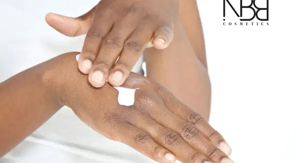 Mani che si applicano crema, per una pelle morbida e liscia. Il logo NB Cosmetics in primo piano.