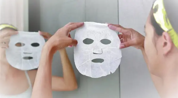 Una donna si prepara per una maschera viso, riflettendosi allo specchio. Scopri quando farla per una pelle radiosa.