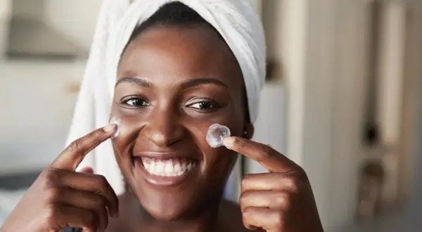 Donna sorridente con turbante applica crema sul viso, un'immagine che evoca il desiderio di vedere i risultati del **retinolo prima e dopo**.