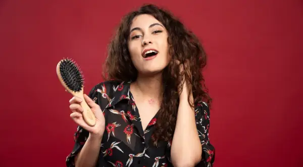 Ragazza con capelli ricci pettinati, tiene in mano una spazzola per capelli.