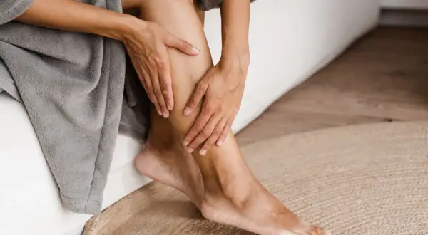 Mani che accarezzano una gamba, un gesto che suggerisce come avere gambe lisce e curate, avvolte in un morbido accappatoio.