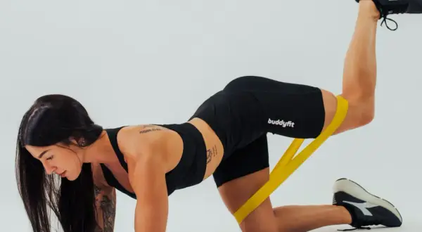 Allenamento per come avere un bel sedere: donna con elastico giallo esegue un esercizio di sollevamento gamba.