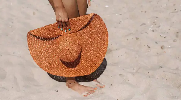 Donna con cappello di paglia arancione sulla sabbia, un'idea per come mantenere l'abbronzatura.