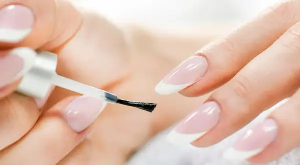 Mani perfette con la manicure a casa. Smalto trasparente applicato con cura su unghie con french manicure.