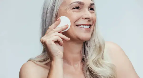 Donna sorridente con cotone per la pulizia del viso, mostrando la differenza tra latte detergente e detergente viso.