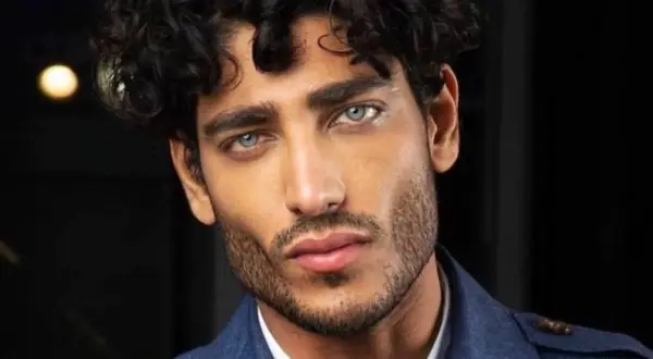 Uomo con capelli mossi scuri e occhi azzurri penetranti, un look che ispira su come farsi i capelli mossi uomo.
