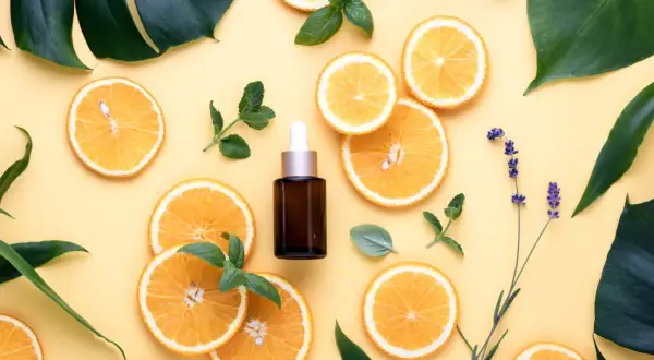 Siero viso con niacinamide e vitamina c, circondato da fette d'arancia, foglie verdi e lavanda.