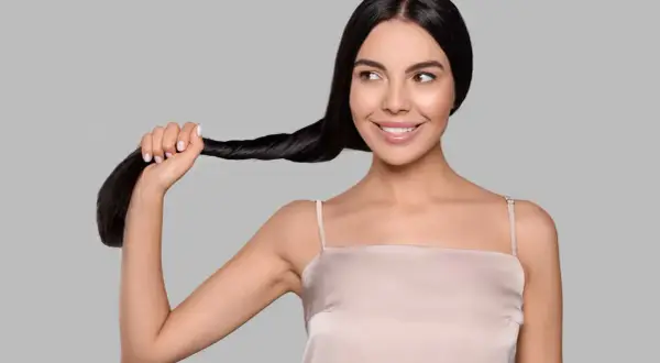 Una donna sorride mentre tiene una ciocca dei suoi lunghi capelli neri. Sembra che si chieda: "henne cos'è?
