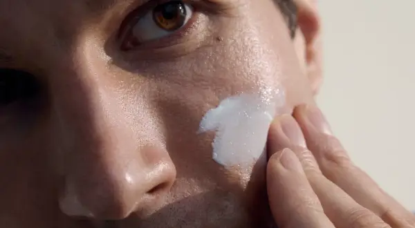 Primo piano di un uomo che applica crema sul viso. La cura della pelle per la pulizia viso uomo è un gesto di benessere.