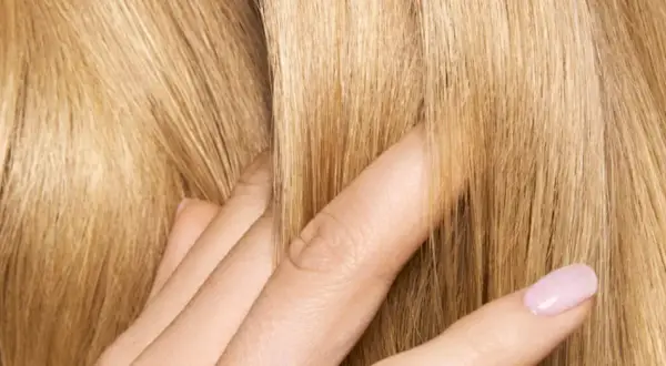 Dita accarezzano capelli biondi e setosi. Posso usare la maschera per capelli prima dello shampoo per ottenere questa morbidezza.