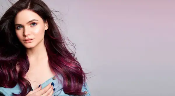 Modella con capelli viola prugna scuro che sfumano in tonalità più chiare, occhi verdi e trucco audace.