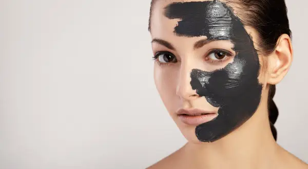 Donna con maschera al carbone sul viso, per scoprire i benefici di una pelle purificata e luminosa.