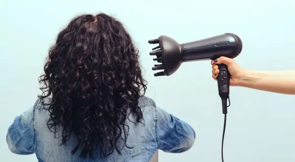 Donna con capelli ricci scuri viene asciugata con diffusore. Scopri come asciugare i capelli ricci per un risultato perfetto.