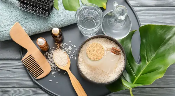 Ingredienti naturali per la cura dei capelli: riso, acqua, oli essenziali, pettine e spazzola. L'acqua di riso capelli è un segreto di bellezza.