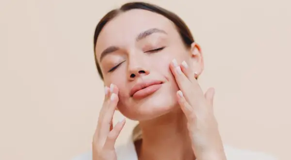Donna con occhi chiusi applica delicatamente una crema sebo regolatrice sul viso, godendosi un momento di cura della pelle.