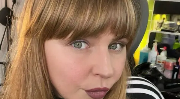 Ragazza con capelli castani e una frangia che incornicia il viso. Sguardo intenso e labbra color prugna.