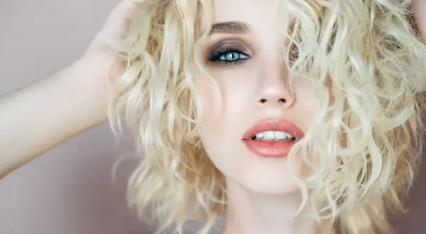 Capelli biondi e ricci, luminosi come la camomilla, incorniciano un volto con occhi azzurri e labbra sensuali.