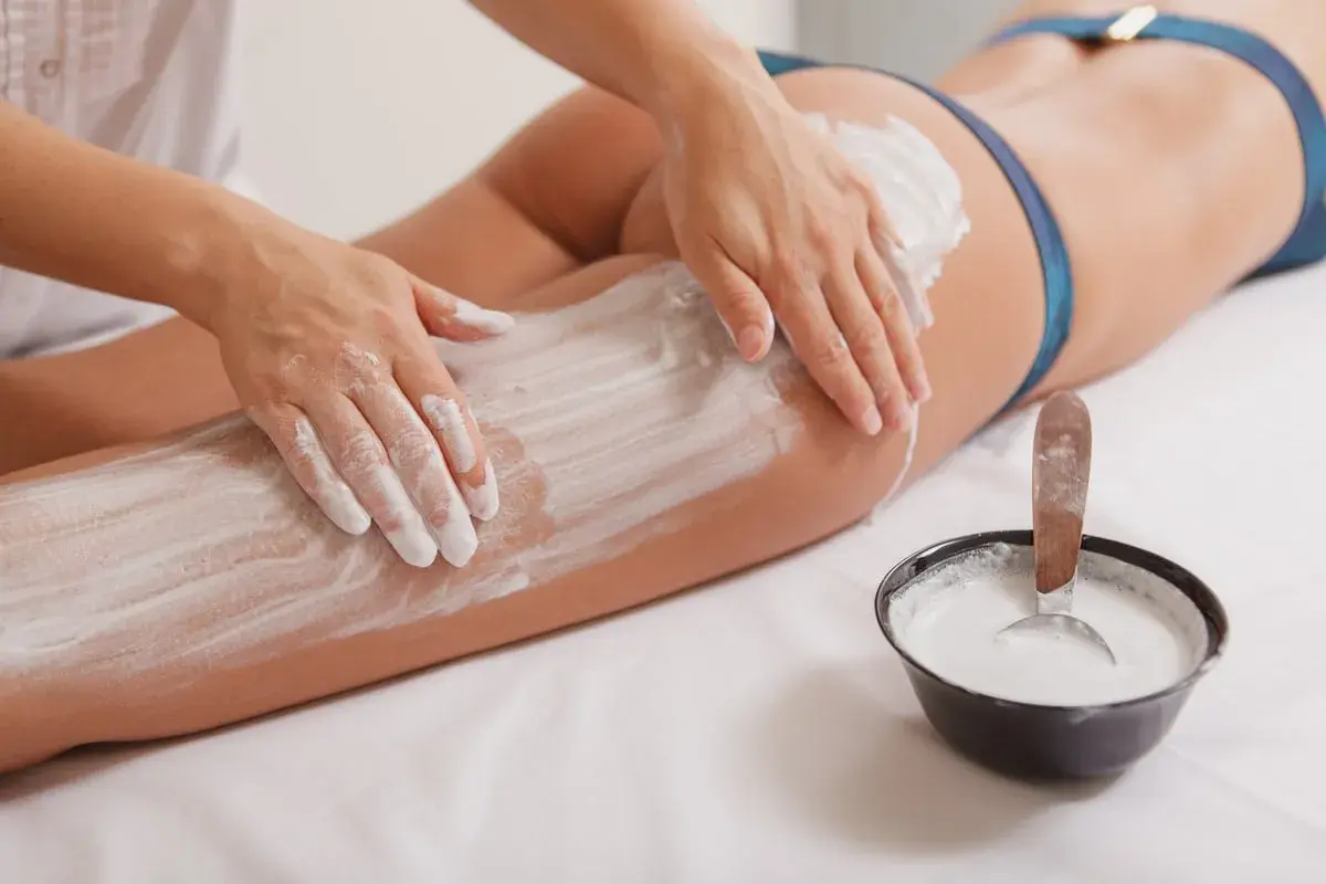 Mani esperte applicano fanghi drenanti su gambe e glutei, un trattamento che promette di aiutare a dimagrire e rimodellare il corpo.