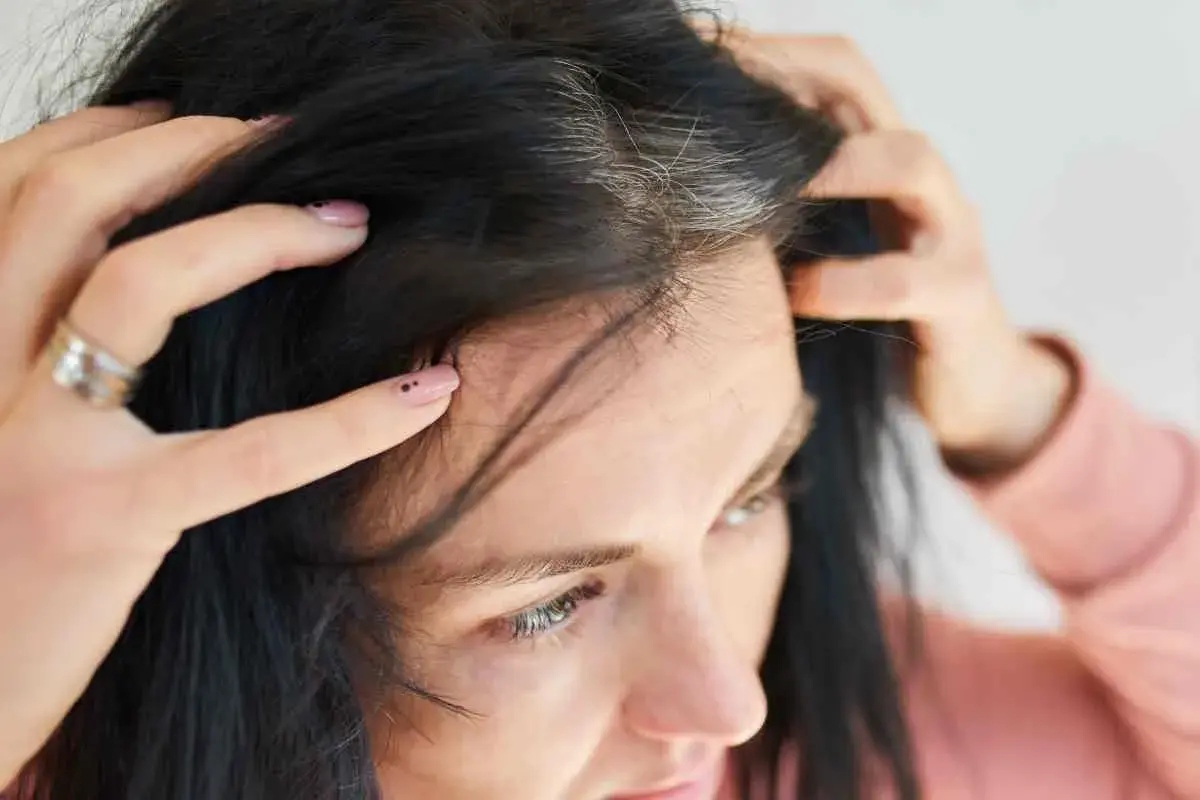 Mani che toccano i primi capelli bianchi tra i capelli scuri, un segno del tempo che passa.