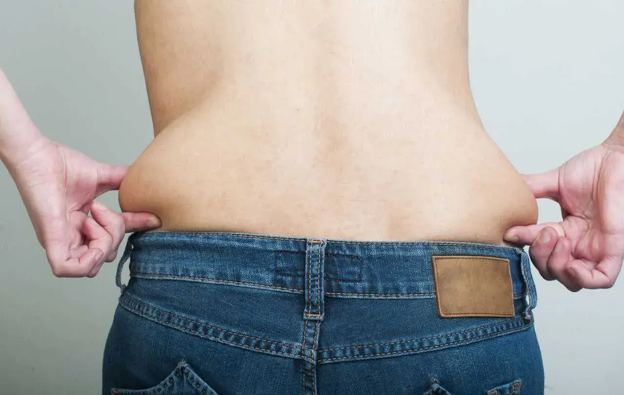 Mani che stringono i fianchi larghi di un uomo, evidenziando accumuli di grasso sopra i jeans.