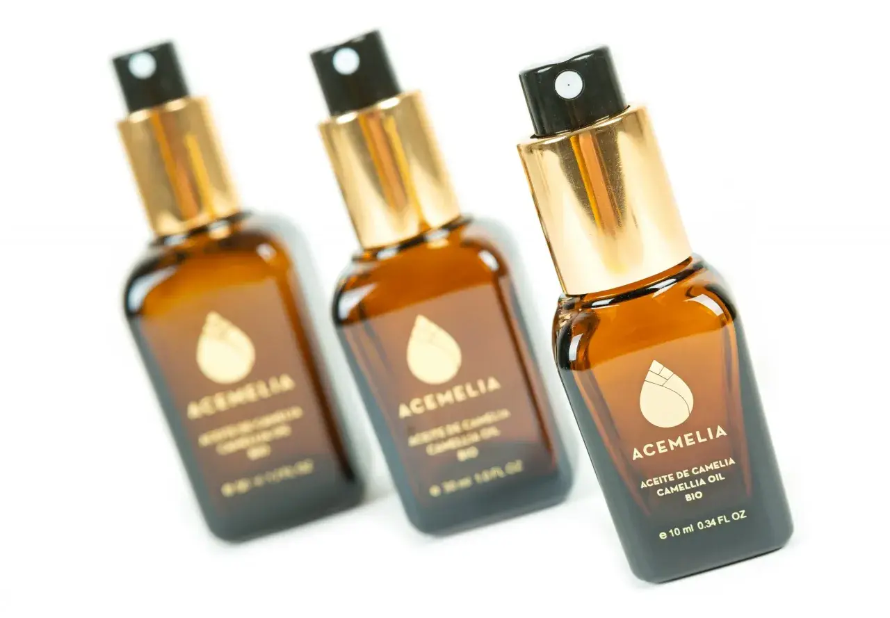 Tre flaconi di olio di camelia per capelli, con tappo dorato e spruzzino nero, su sfondo bianco.