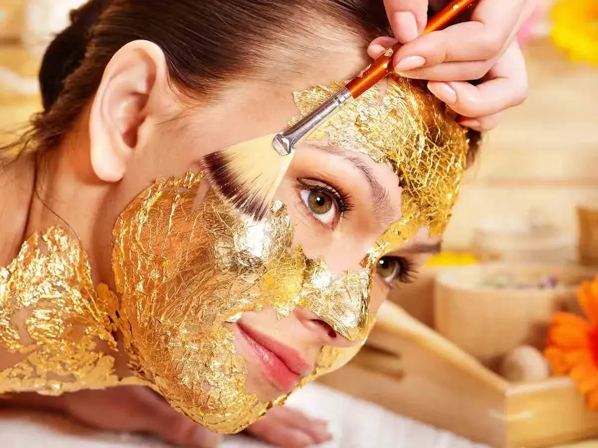 Una donna riceve un trattamento di bellezza con una maschera viso oro, scoprendo i suoi benefici rigeneranti.