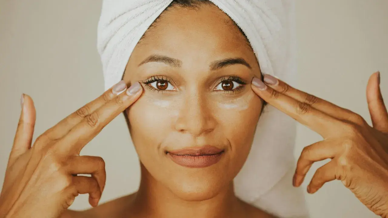 Donna con turbante applica crema contorno occhi, mostrando la differenza tra unguento e crema per la cura della pelle.