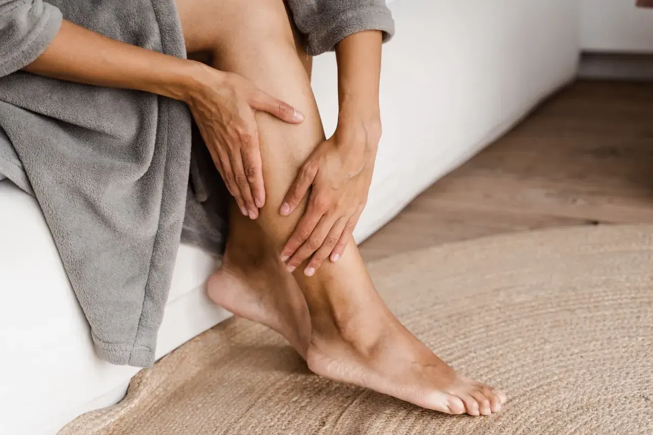 Mani che accarezzano una gamba, un gesto che suggerisce come avere gambe lisce e curate, avvolte in un morbido accappatoio.