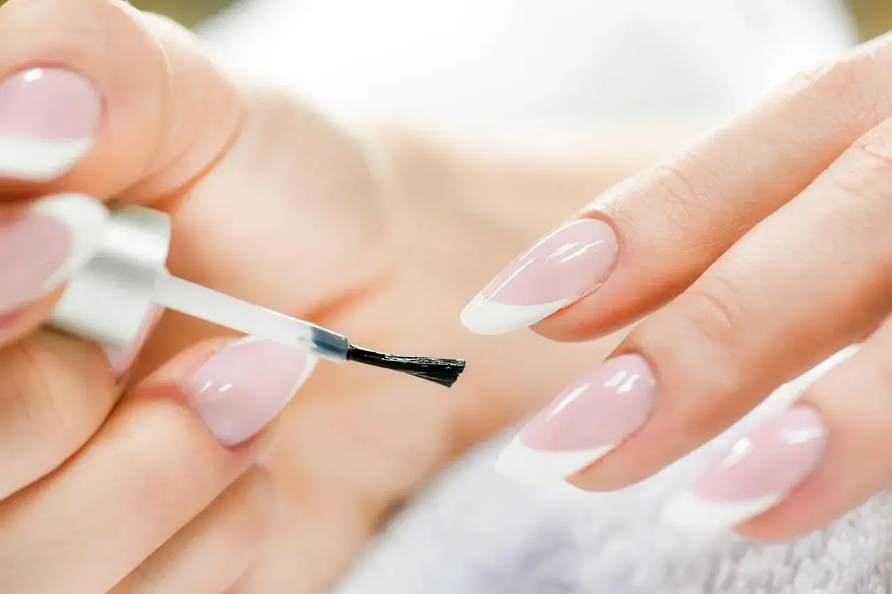 Mani perfette con la manicure a casa. Smalto trasparente applicato con cura su unghie con french manicure.