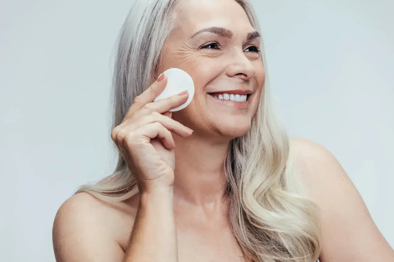 Donna sorridente con cotone per la pulizia del viso, mostrando la differenza tra latte detergente e detergente viso.