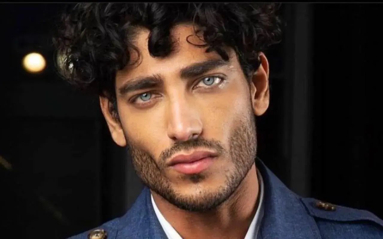 Uomo con capelli mossi scuri e occhi azzurri penetranti, un look che ispira su come farsi i capelli mossi uomo.