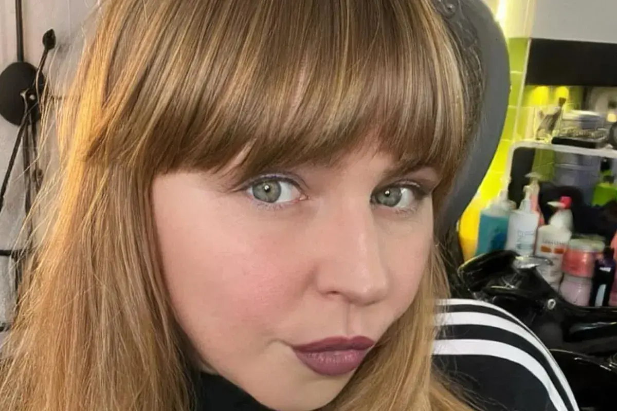 Ragazza con capelli castani e una frangia che incornicia il viso. Sguardo intenso e labbra color prugna.