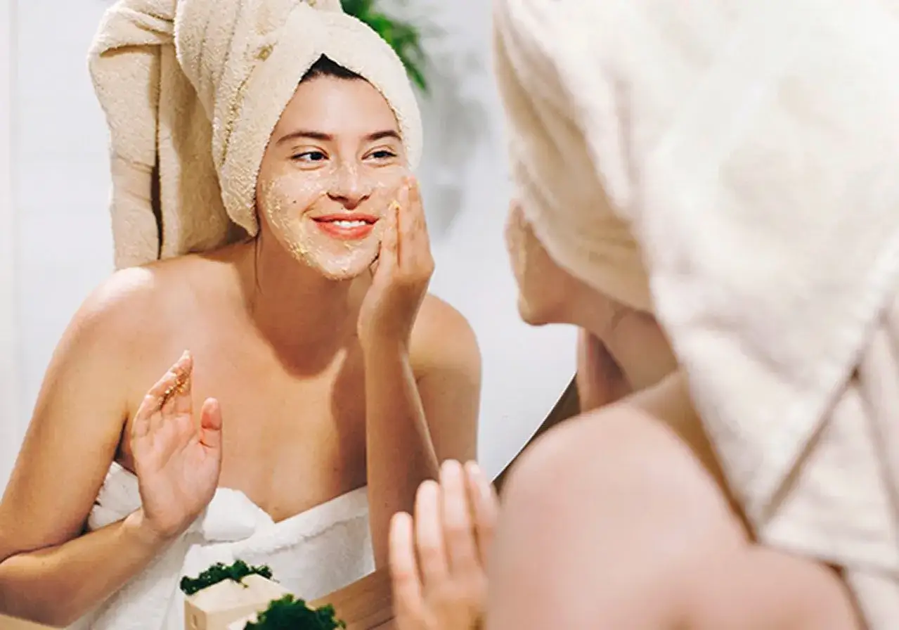 Ragazza sorridente si applica uno scrub viso, scoprendo cos'è lo scrub per una pelle luminosa.