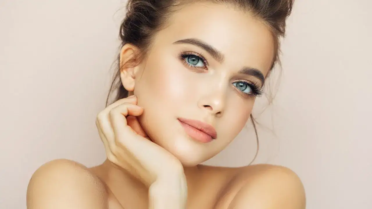 Primo piano di un volto femminile con un occhio incappucciato trucco impeccabile, ciglia lunghe e labbra morbide.