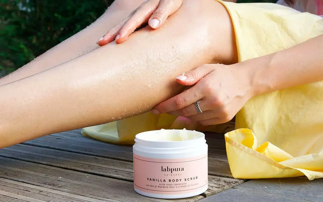 Mani che applicano gommage corpo rigenerante Labpura, con cristalli di zucchero e olio di mandorle dolci, per una pelle liscia e luminosa.