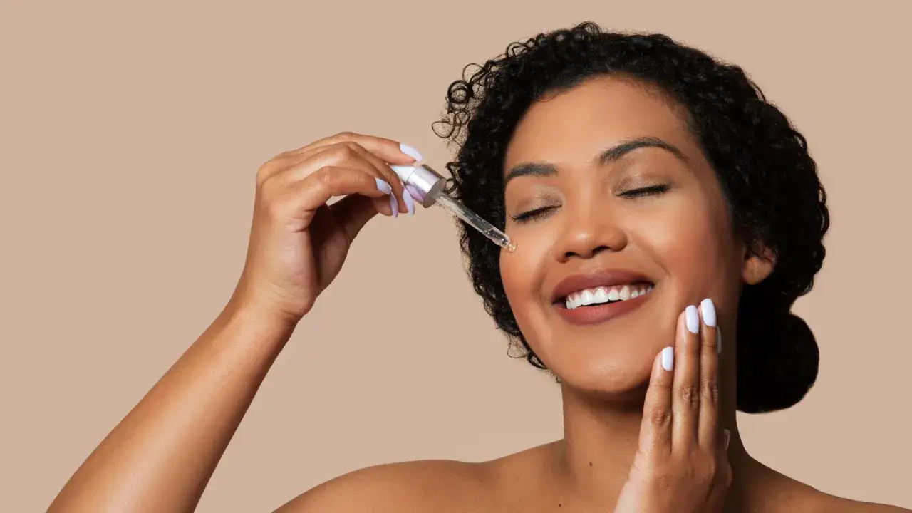Donna sorridente applica siero vitamina c quando usarlo, con gli occhi chiusi e una goccia sul viso.